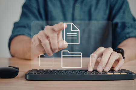 An individual is seen interacting with virtual file icons displayed on a computer screen. The person is using touch gestures to manipulate the icons, which include a document and folders. The scene is set on a wooden desk with a keyboard and mouse visible.の写真素材