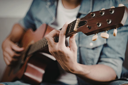 A close-up image of a person playing an acoustic guitar, focusing on their hands on the instrument.