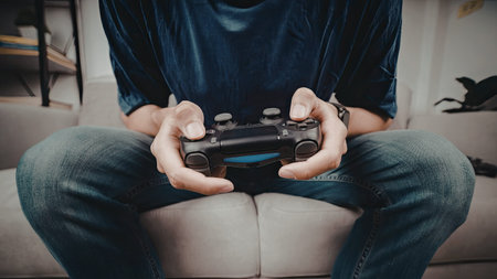 A person is seated on a couch, holding and using a video game controller, likely engaged in a gaming...