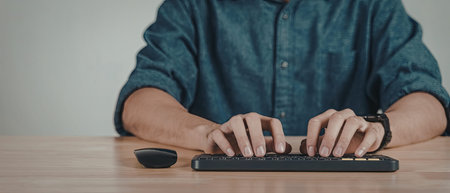 A close-up image of a person's hands typing on a computer keyboard. The individual is wearing a blue...