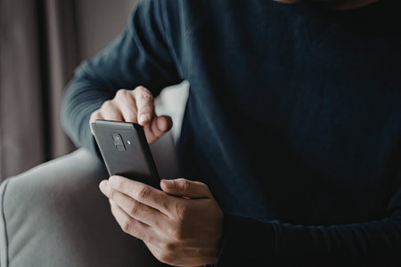 A person wearing a blue sweater is seated comfortably, engrossed in using a smartphone. The focus is...