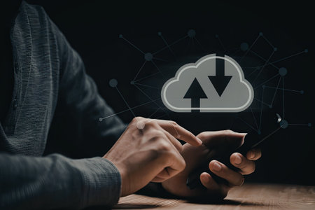 A person is using a smartphone while a cloud with a download icon hovers above it, indicating data transfer or cloud storage activity.の写真素材