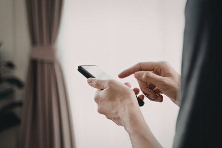 A close-up image of a person's hands holding and interacting with a smartphone while standing near a...