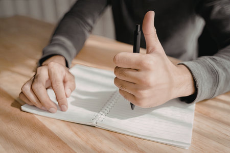 A close-up image of a person's hands writing in a notebook with a pen.の写真素材