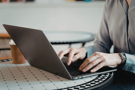 A person is working on a laptop at a cafe, with a cup of coffee and a book nearby.