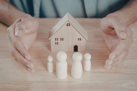 A wooden house model is surrounded by small wooden figures, symbolizing family protection and insurance.の写真素材