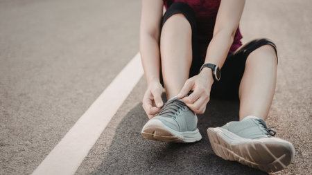 A person is seated on the road, adjusting their shoe laces before running. The individual is wearing athletic clothing and running shoes.の写真素材