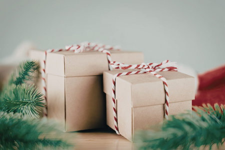 Three small brown gift boxes tied with red and white string, placed on a surface with green foliage...
