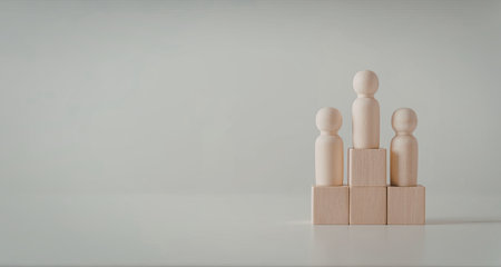 Three wooden figures standing on top of wooden cubes against a plain background.の写真素材