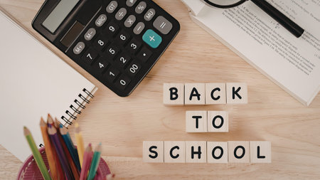 An image featuring wooden blocks arranged to spell 'BACK TO SCHOOL' on a wooden desk. The desk also...