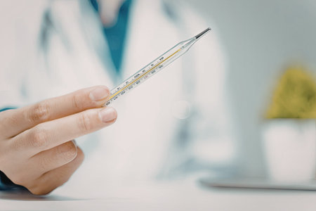 A close-up image of a doctor holding a medical thermometer, likely preparing to take a patient's...