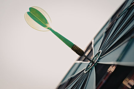 A close-up image of a green dart successfully hitting the bullseye on a dartboard. The dart is prominently featured with the dartboard in the background.の写真素材