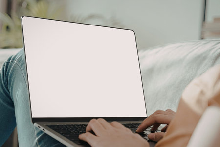 An individual is comfortably seated on a couch, using a laptop computer. The laptop screen is blank,...