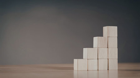 A minimalist arrangement of wooden blocks stacked in a pyramid formation against a dark,...