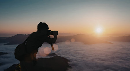 A silhouette of a photographer taking a picture of a stunning sunrise over a foggy landscape with...