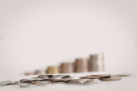 A collection of coins arranged in stacks, with varying sizes and types, set against a plain white...