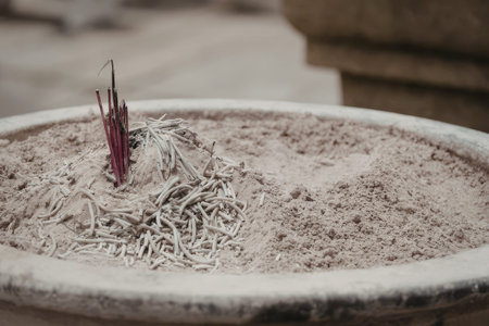 A close-up image of a ceramic bowl containing remnants of burnt incense sticks, with visible ash and...