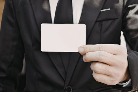 A close-up image of a businessman in a suit holding a blank name card.
