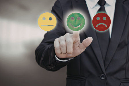 A businessman in a suit is selecting a green happy face emoticon from three options: happy, neutral,...