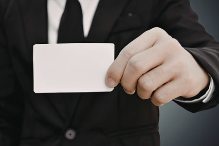 A close-up image of a businessman in a suit and tie holding out a blank business card.