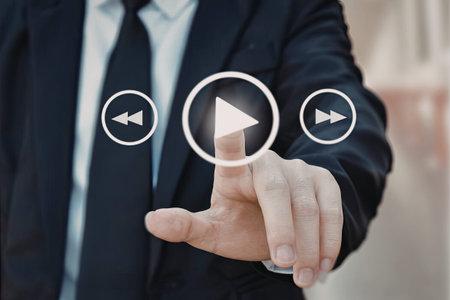 A close-up image of a businessman in a suit pressing a play button on a virtual interface, with...