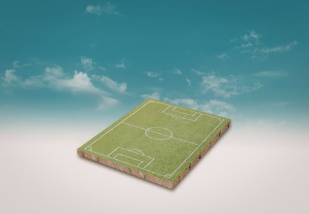 A detailed miniature soccer field set against a bright blue sky with scattered clouds. The field includes the goal posts, penalty areas, and center circle.の写真素材