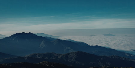 A panoramic view of a mountain range under a clear blue sky. The mountains are partially covered with mist, creating a serene and majestic atmosphere.の写真素材