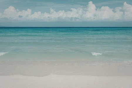 A tranquil beach scene featuring calm turquoise waters gently lapping against the sandy shore under...