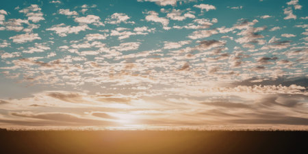 A tranquil image capturing the beauty of a sunset over a calm horizon. The sky is adorned with scattered clouds, and the sun casts a warm glow across the scene.の写真素材