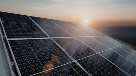 A series of solar panels are angled towards the setting sun, capturing the warm hues of the sky. The...