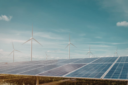 A vast array of solar panels in the foreground with wind turbines standing tall in the background under a clear blue sky.の写真素材