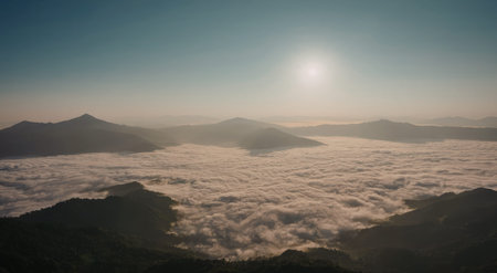A breathtaking view of the sun rising over a range of misty mountains, casting a warm glow across the sky and landscape.の写真素材