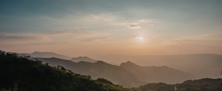 A serene sunrise over a mountain range with misty valleys and lush greenery.