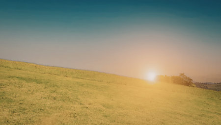 A serene landscape featuring rolling green hills under a clear blue sky with the sun setting in the...