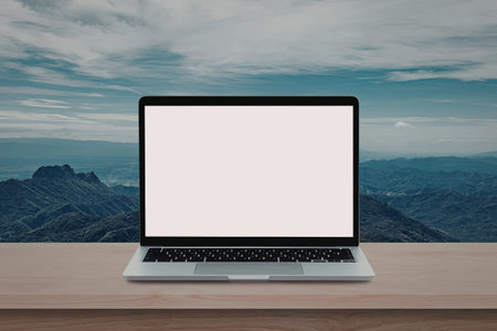 A laptop computer is placed on a wooden surface with a stunning mountain range and cloudy sky in the...