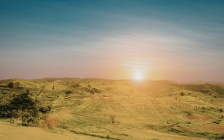 A serene landscape featuring rolling hills bathed in the warm glow of a rising sun. The sky is...