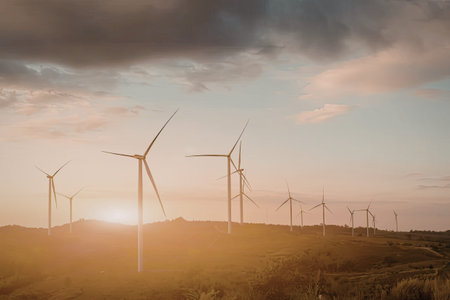 A serene landscape featuring multiple wind turbines silhouetted against a vibrant sunset. The sky is...