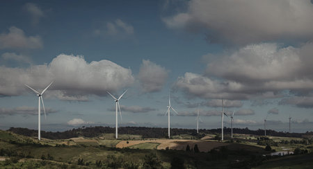 A serene landscape featuring multiple wind turbines standing tall against a backdrop of a partly...