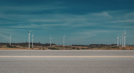 A scenic view of multiple wind turbines standing tall beside a highway under a clear blue sky.の写真素材