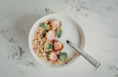 A bowl of granola with fresh strawberries, broccoli and milk on a marble countertopの写真素材