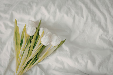 a bunch of white flowers with green leaves on a white crumpled clothの写真素材