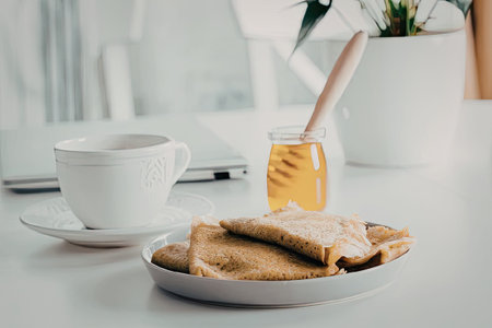 A plate of toast with a jar of honey and a cup of coffee on a white tableの写真素材