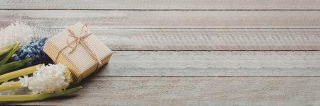A small gift box wrapped with brown twine lies next to a bouquet of white and purple flowers on a rustic wooden surface.の写真素材