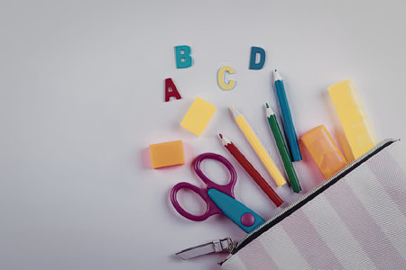 A collection of school supplies including letters, erasers, scissors, pencils, and markers spilling out of a striped pouch.の写真素材