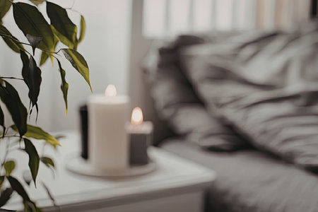 A serene and peaceful bedroom scene with lit candles on a bedside table, a comfortable bed, and a plant adding a touch of greenery.の写真素材