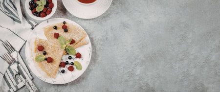 A plate of crepes with fresh berries and a bowl of mixed berries on a table with a cup of coffeeの写真素材