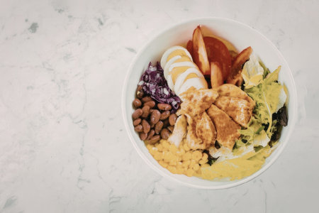 A nutritious bowl filled with chicken, rice, beans, and various vegetables.の写真素材