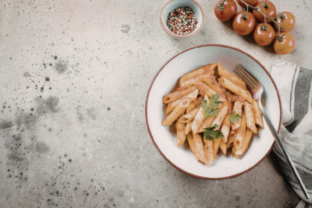 A plate of penne pasta with tomato sauce and herbs on a concrete background with tomatoes and spicesの写真素材