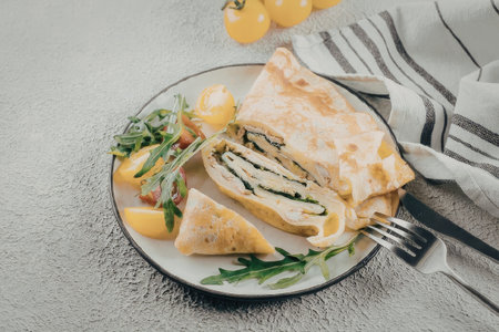A crepe filled with spinach and cheese, served with a side salad and fresh vegetables on a plate.の写真素材