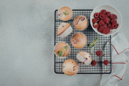 A cooling rack with muffins and a bowl of raspberries on a tableの写真素材